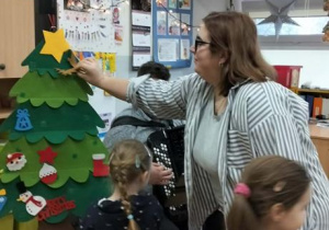 Nauczycielka z dziećmi dekorują choinkę