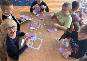 Dzieci wykonują prace plastyczna. Nawlekają włóczkę na rękawiczki