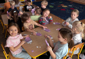 Dzieci wykonują prace plastyczna. Nawlekają włóczkę na rękawiczki