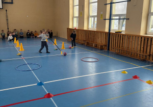 Dzieci toczą piłkę kijem hokejowym między pachołkami