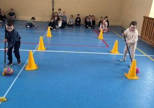 Dzieci biorą udział w konkurencji sportowej tocząc piłkę