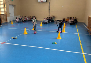 Dzieci biorą udział w konkurencji sportowej tocząc piłkę