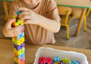 chłopiec wznosi budowlę z plastikowych klocków