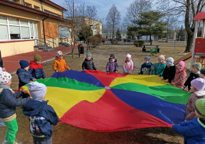 Dzieci bawią się kolorową chustą animacyjną na świeżym powietrzu.