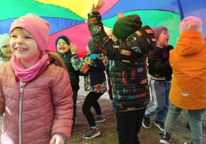 Przedszkolaki wspólnie bawią się chustą animacyjną na trawie.