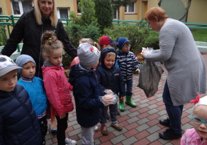 Dzieci zakładają rękawiczki, aby sprzątać teren wokół przedszkola