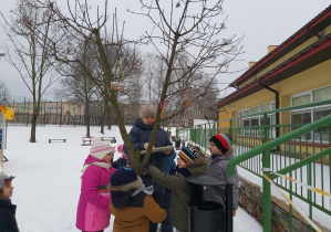 Zawieszanie przez dzieci ciasteczek na drzewkach