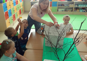 Przedszkolaki i nauczycielka doczepiają liście